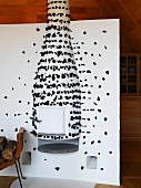 Kaminofen im weissen Raumteiler eingebaut und mit schwarzen Papierfetzen dekoriert