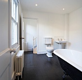 Traditional bathroom in old building with free-standing, claw-footed bathtub on black tiled floor