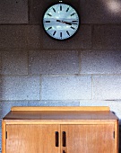 Wall clock and fifties cabinet against unrendered, concrete block wall