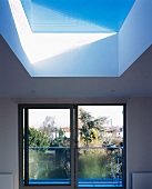 Unframed skylight and wide, floor-to-ceiling sliding window with steel and glass balustrade