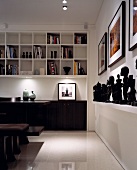 Designer dining area in dark, tropical wood contrasting with white-painted shelving and glossy floor tiles
