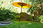 Gelber Sonnenschirm aus Papier, große Schale aus Stein und Buddhakopf auf einer Gartenwiese