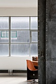 View through open sliding door into room with orange shell chair below industrial window