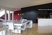 White modern dining table and chairs in front of free-standing kitchen island and black fitted cupboards in open-plan interior