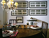 Place settings and filled wine glasses on wooden table in front of wall with framed pictures