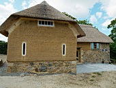 Rustic building in organic style with thatched roof above clay and stone facade