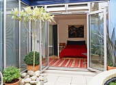 Kleine Innenhof-Terrasse im zeitgenössischen Stil und Blick auf Doppelbett mit knallroter Tagesdecke