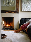 Large mirror above fire in fireplace and feet on white fur rug