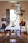 weiße Tischdecke auf Tisch und farbig lackierte Stühle vor Fenster im traditionellen Wohnzimmer