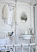 Vintage washbasin and jug on metal stand and shirt on clothes hanger on white-painted wooden wall