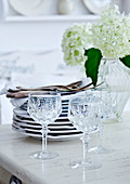 Crystal wine glasses in front of stacked plates and white flowers in glass vase