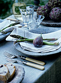Place setting with fig and green asparagus on linen napkin and rustic stone plate
