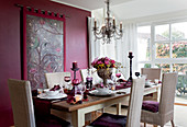 Festlich gedeckter Esstisch mit Rattanstühlen vor purpurfarbener Wand mit Wandbehang