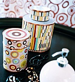 Containers with a colorful pattern next to a necklace on a black tray