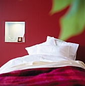 Bett mit weissen Kissen vor rot getönter Wand
