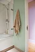 Towel on wall hook next to bathtub and open door in small bathroom