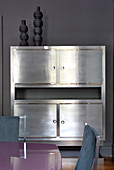 Elegant silver cabinet against grey wall; glossy table and leather-covered dining chairs in foreground