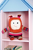 Hand-sewn fantasy figure rag doll with crooked features sitting on pink and blue nursery shelves