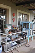 Shelves holding various collectors' items such as old typewriters, watering cans etc. on veranda