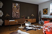 Cow skin rug next to shell chair at desk and dark brown wall in 70s-style room