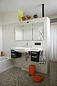 Waschbecken mit Spiegel an weiss gefliestem Raumteiler im Bad mit Terrazzoboden