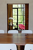 Massivholztisch und Stühle mit weisser Lehne im Esszimmer vor offenem Durchgang und Blick auf Fensterfront mit Gartenaussicht