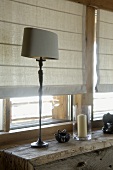 Table lamp on rustic cabinet against window with half-closed blinds