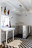 Black and white floor tiles and old Delft tiles in the bathroom of a country house with exotic masks hung above a retro, free-standing wash stand
