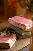Antique, tattered books on a wooden surface and a pair of modern reading glasses