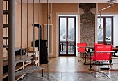 Gemütlicher Wohnraum in Chalet mit rustikaler Steinwand, Kaminofen, gläsernem Esstisch und roten Drehstühlen