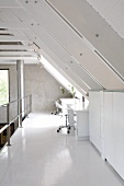 Home office on loft apartment mezzanine below white-painted rafters with light falling through dormer window
