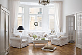 Sofagarnitur mit weissen Hussen und Couchtisch unter Kronleuchter im Wohnzimmer-Erker einer Altbauwohnung