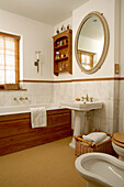 Traditional country house bathroom with wood-panelled bathtub and decorative oval mirror above pedestal washbasin