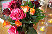 Colourful bouquet of roses and lit tealights on table