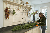 Woman tying festive garland of fir branches on dark worksurface in cream-coloured country house kitchen