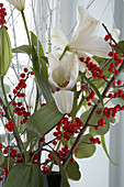 Christmas bouquet of white lilies and twigs of red berries in front of window