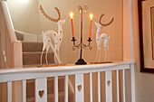 Advent arrangement of stylised stags and candelabra with lit candles on wooden landing balustrade in country house