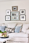 Framed black and white photographs above pale, country house sofa with scatter cushions