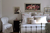 Rose-patterned cushions and pillows on metal bed with antique-inspired elements below framed painting of roses on wall