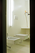 Minimalist bathroom with vertical fluorescent tubes above square designer toilet and bidet