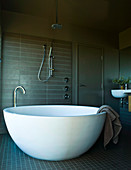 Free-standing, white designer bathtub shaped like half an eggshell in masculine bathroom
