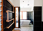 View from sauna into black-tiled designer bathroom with free-standing bathtub through open glass door