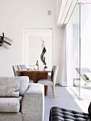 Blick über grauem Polstersofa auf Esstisch aus Nussholz und gepolsterte Stühle vor Glasfassade in Designer Wohnzimmer