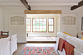 Offener Ess-und Wohnbereich mit weissen Wänden und Holzboden; Blick in das Nebenzimmer mit Sprossenfenstern
