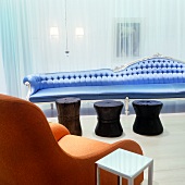 Eclectic mix of styles in Postmodern London hotel lounge - rustic wooden stools in front of delicate, extra-long sofa covered in sky-blue satin and plain, apricot armchair next to functional metal table