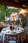 Dinner in a courtyard - candle lanterns on set table in front of climber-covered house facade
