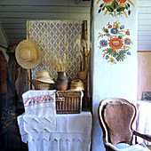 Embroidered linen, baskets and straw hats on table; cheerful and simple, rustic floral mural on chimney flue