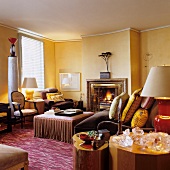 Various upholstered furniture in front of open fireplace in yellow-painted living room with traditional ambiance