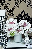 White hydrangeas in small vase against brocade flock wallpaper