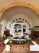 View across antique table into Mediterranean living room with barrel-vaulted ceiling and wall plates around arched doorway